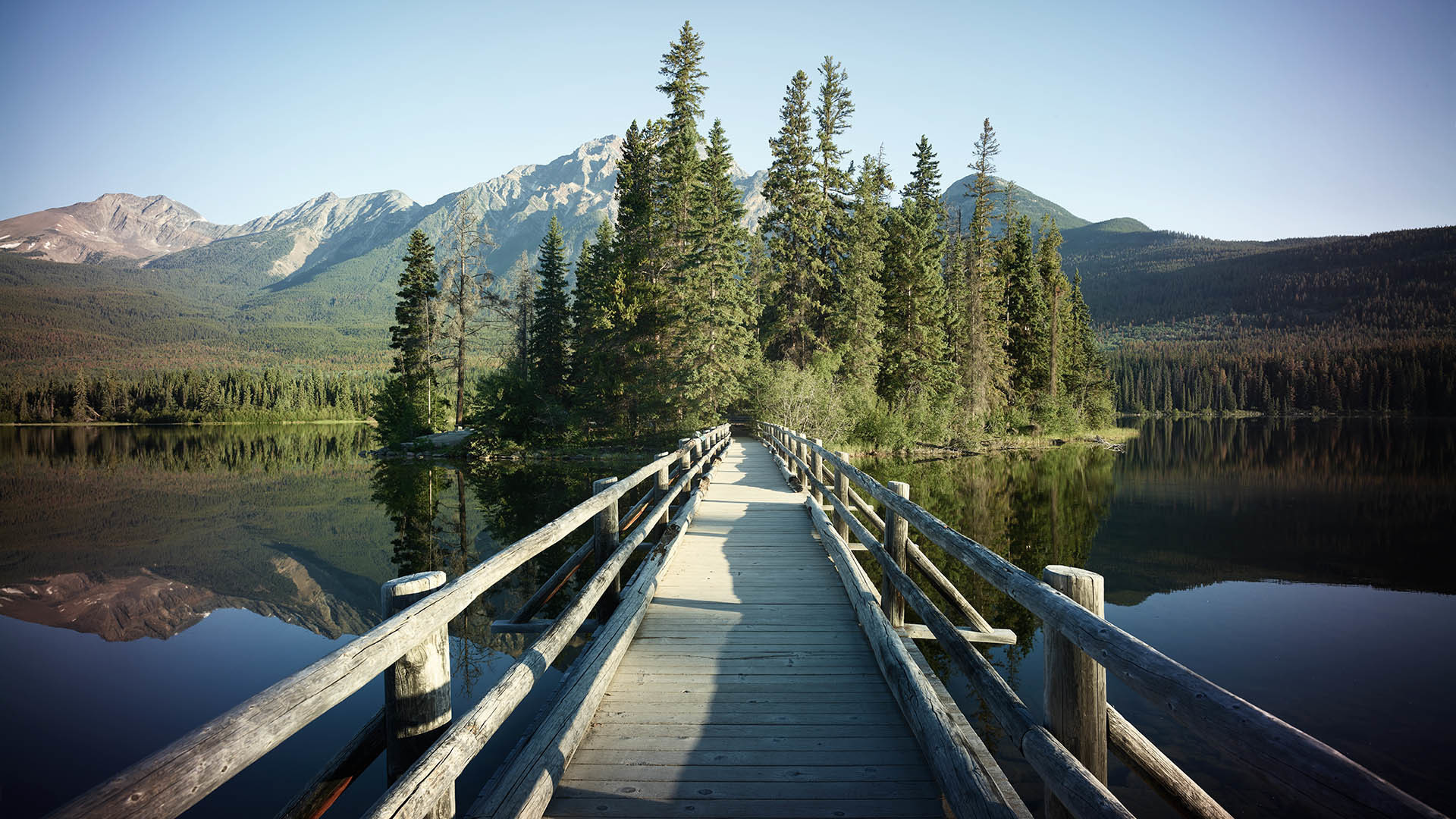Wooden bridge over mountain lake with fir forest on bank